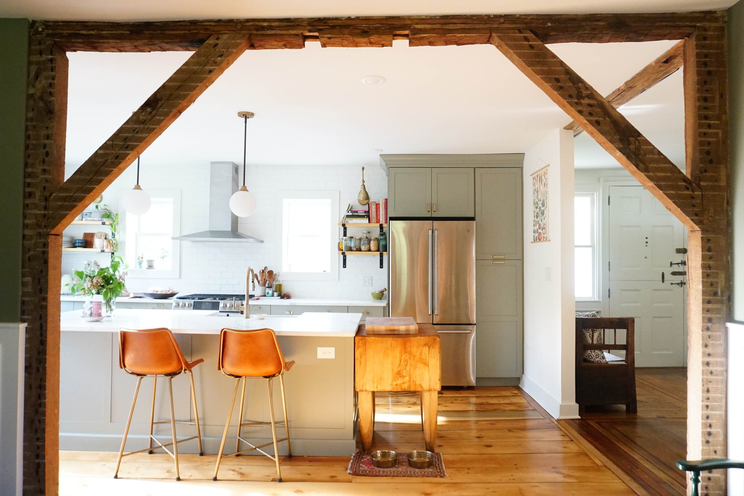 Open kitchen framed by original rustic timber beams, with orange leather counter stools: 1790 Farmhouse Renovation, Milton NY